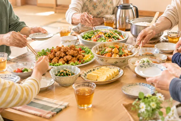 大皿料理が並ぶ長机に、いろいろな世代の人の手が伸びている食卓